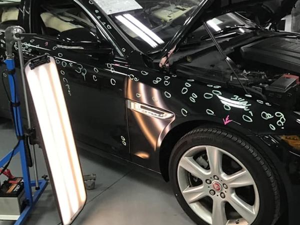 Black Jaguar with hail dents circled on the hood and fender